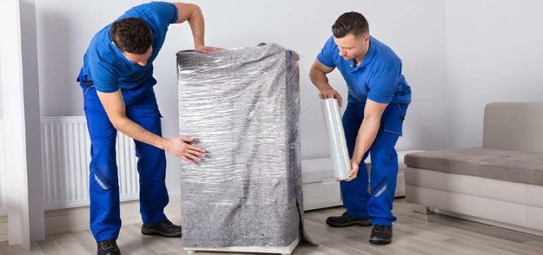 Two workers in blue uniforms securely wrap a large item in plastic for transport. Safe Packaging in Shipping and Logistics.
